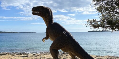 A dinosaur sculpture on a rocky shoreline with the Adriatic sea in Premantura, cape Kamenjak, Istria
