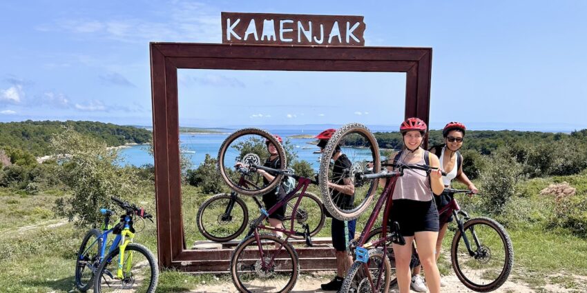 People with bikes near a 'KAMENJAK' sign overlooking the sea and greenery in Premantura near Pula, Istria in Croatia.